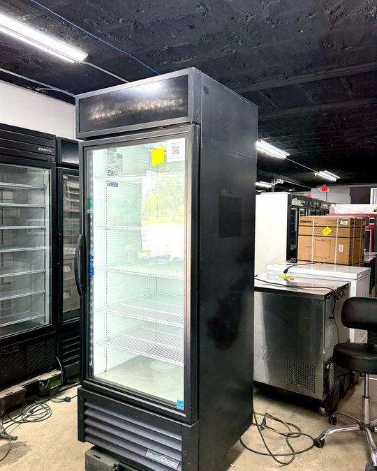 A lit True 1-door glass door merchandiser on the showroom floor.